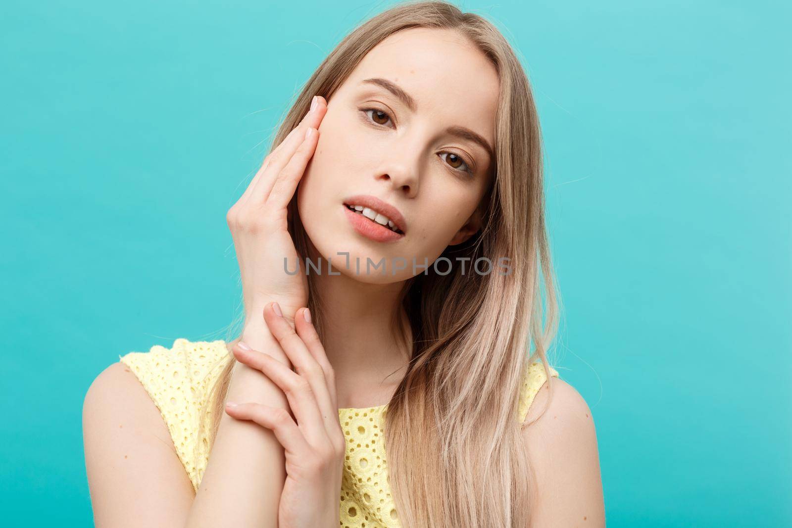 Beautiful Woman Face Portrait Beauty Skin Care Concept: beauty young caucasian female model girl touching her face skin cheeks hands fingers. Fashion Beauty Model isolated on blue