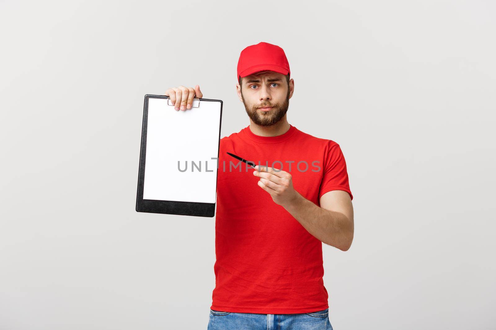 Delivery Concept: Portrait Young caucasian Handsome delivery man or courier showing a confirmation document form to sign. Isolated on Grey studio Background. Copy Space. by Benzoix