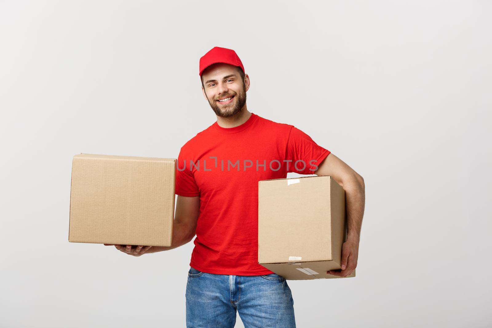 Delivery Concept: Smiling handsome caucasian delivery man holding a paper box. Isolated over grey background