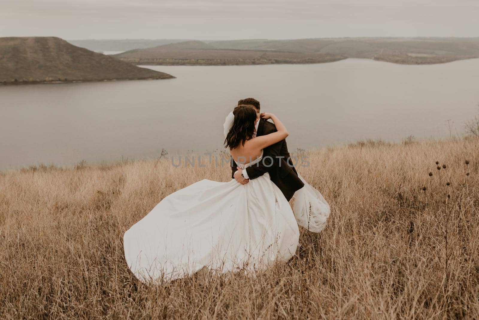 couple wedding newlyweds in walk hug kissing on tall grass on mountain above the river by AndriiDrachuk