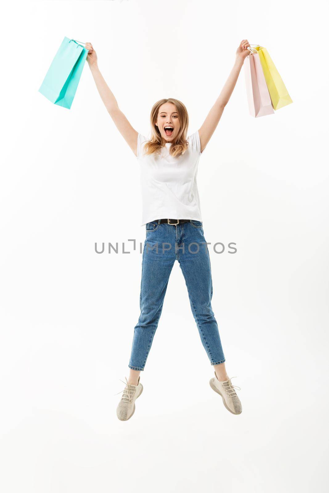 Full length portrait of a happy pretty girl holding shopping bags while jumping and looking at camera isolated over white background.