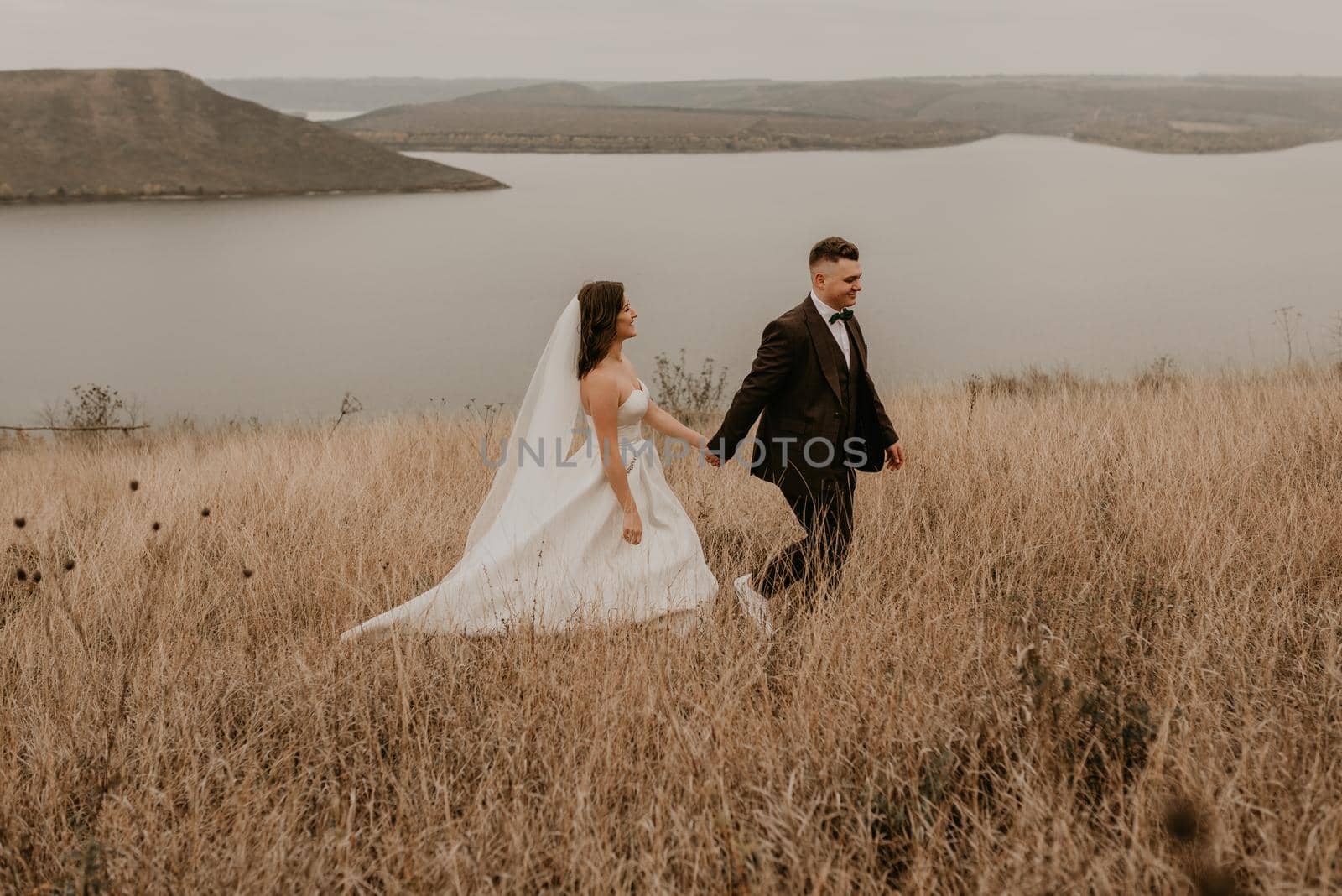 couple wedding newlyweds in walk hug kissing on tall grass on mountain above the river by AndriiDrachuk