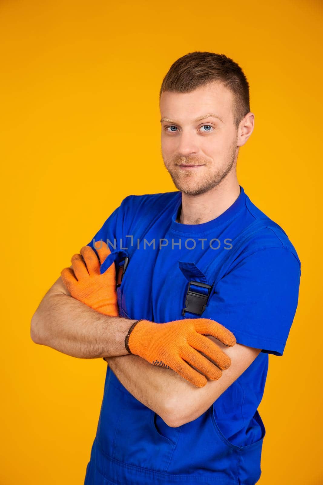 Young male worker in gloves and overalls. Male repair specialist. Professional for work. Yellow background