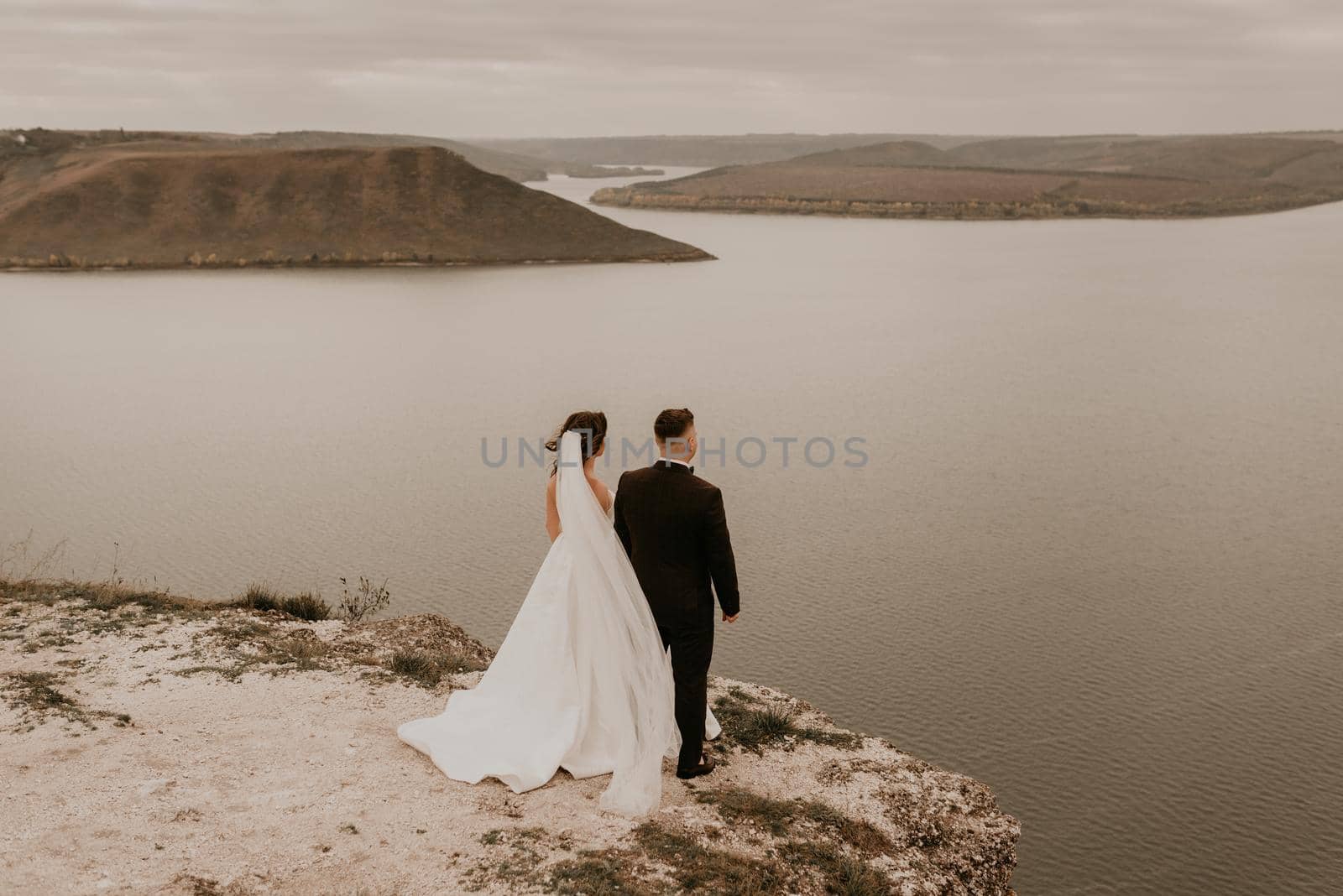 loving couple wedding newlyweds outdoor. bride in white dress long veil and groom in suit walk in summer fall on mountain above river. sunrise. man and woman on rocks above cliff. bakota ukraine