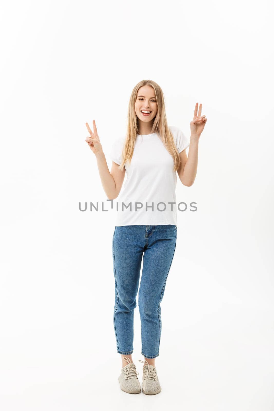 Full length portrait of a happy young woman standing and showing peace gesture with two hands isolated over white background.