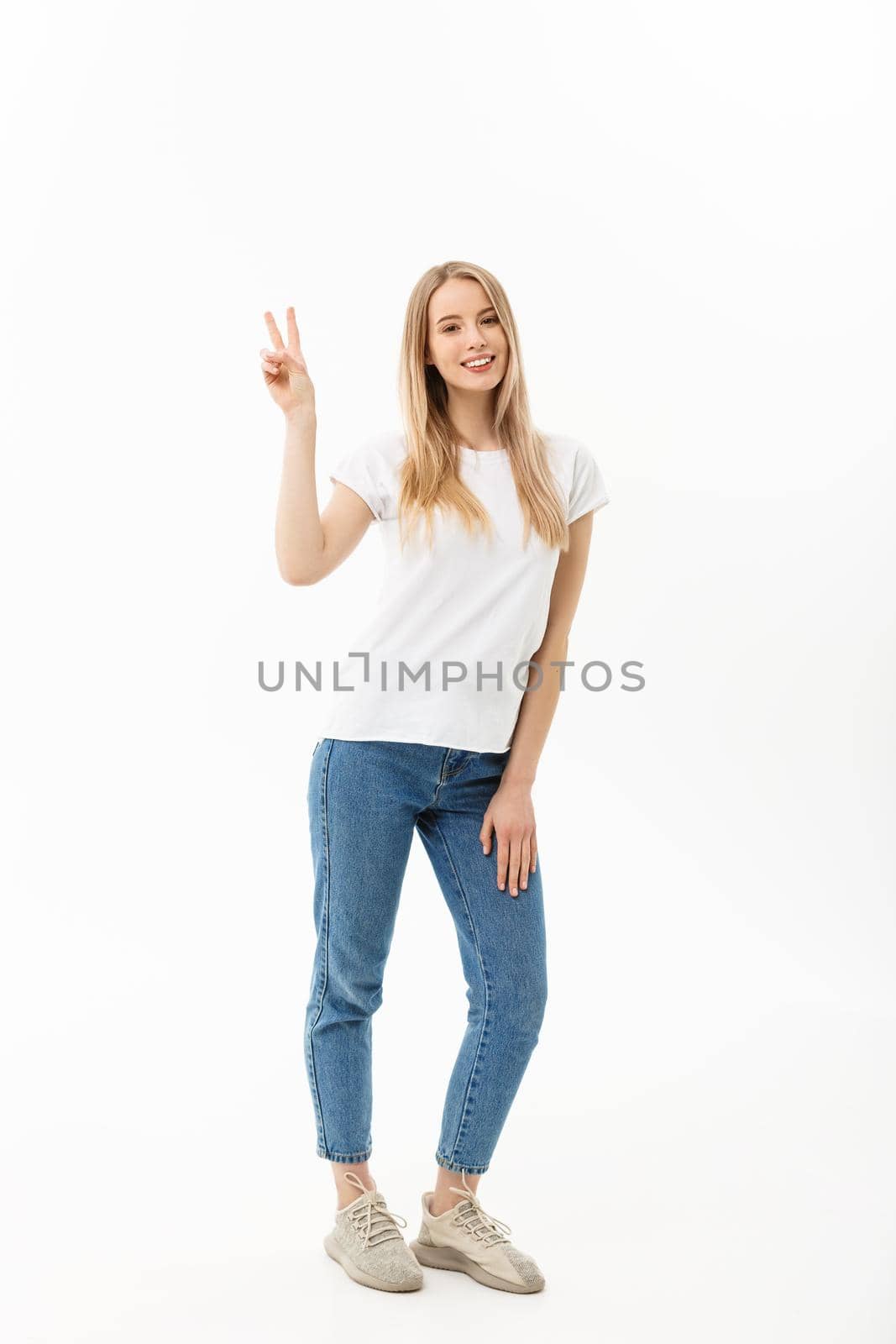 Full length portrait of a happy young woman standing and showing peace gesture with two hands isolated over white background.