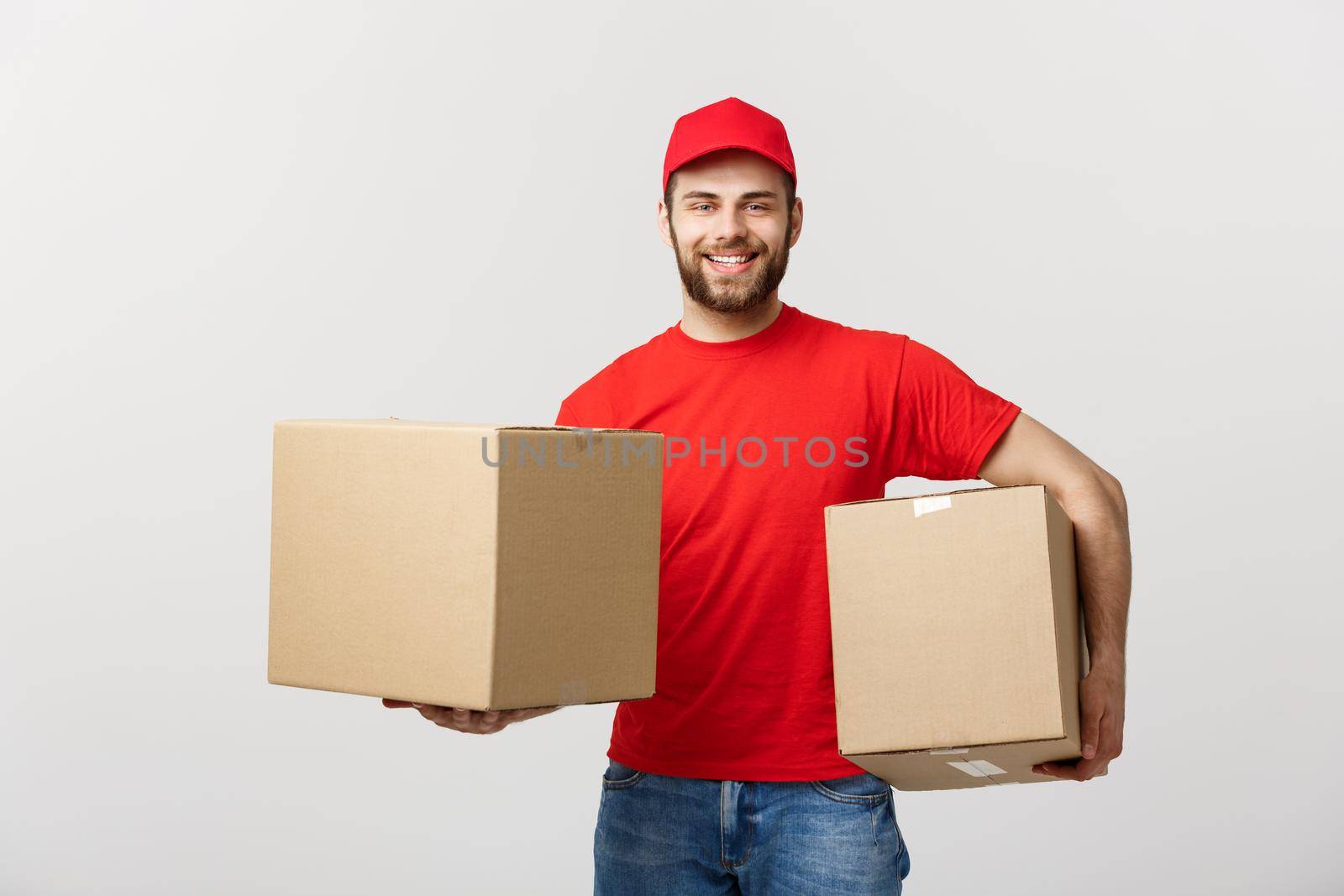 Delivery Concept: Smiling handsome caucasian delivery man holding a paper box. Isolated over grey background