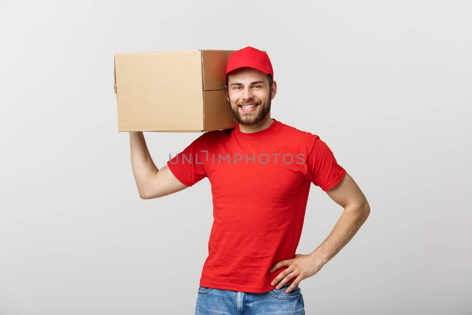 Deliver Concept: Young caucasian handsome delivery man holding a box on shoulder. Isolated over grey background