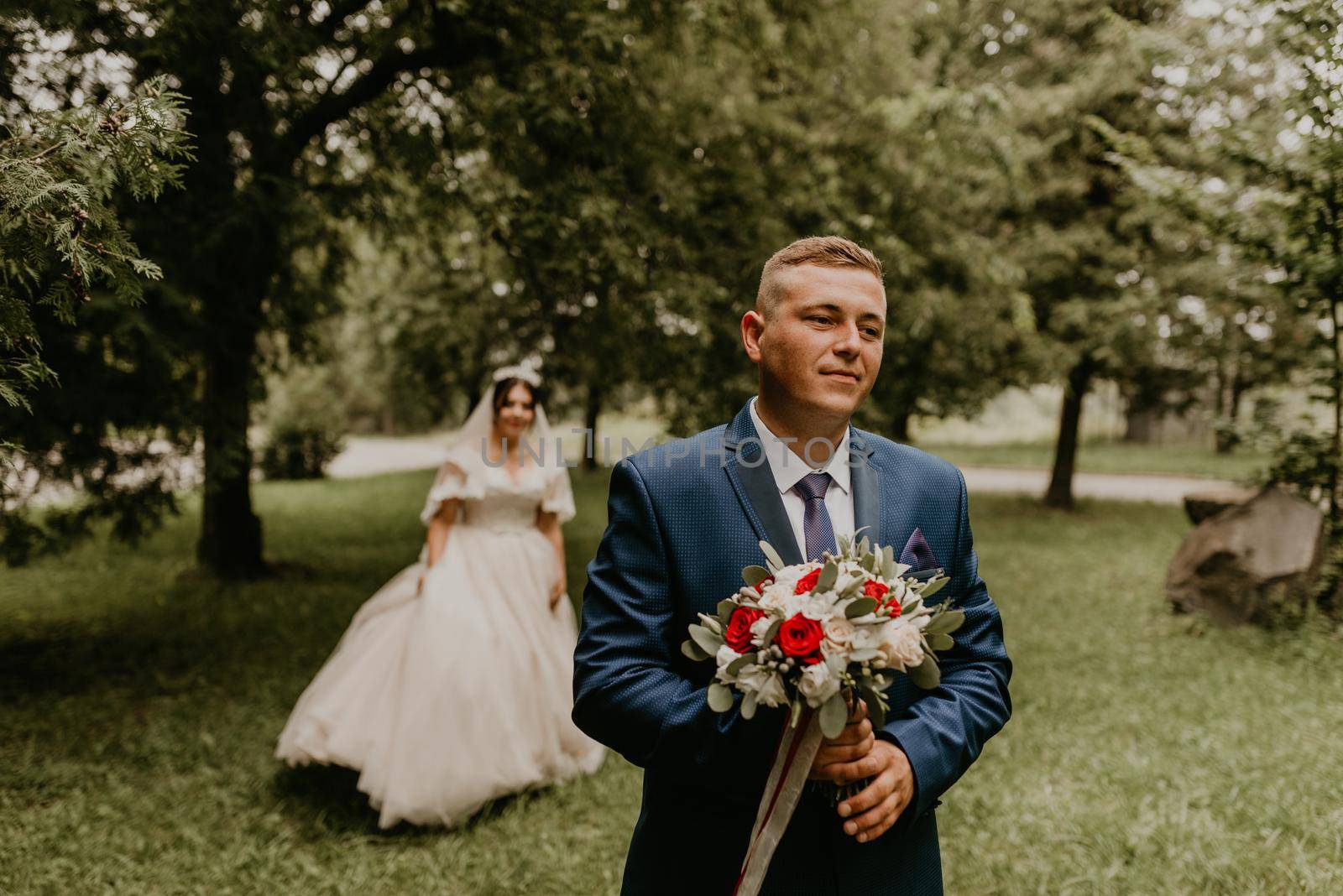 blonde European Caucasian young man groom in blue suit and black-haired woman bride in white wedding dress with long veil and tiara on head. first meeting newlyweds groom wait sees bride