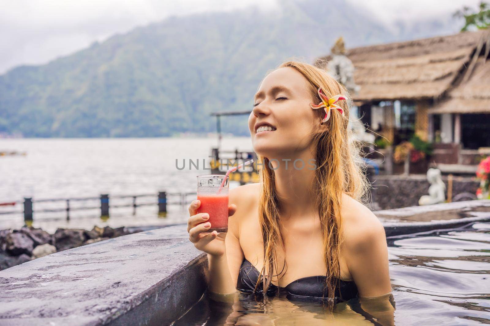 Geothermal spa. Woman relaxing in hot spring pool against the lake. hot springs concept. Drinking guava juice.