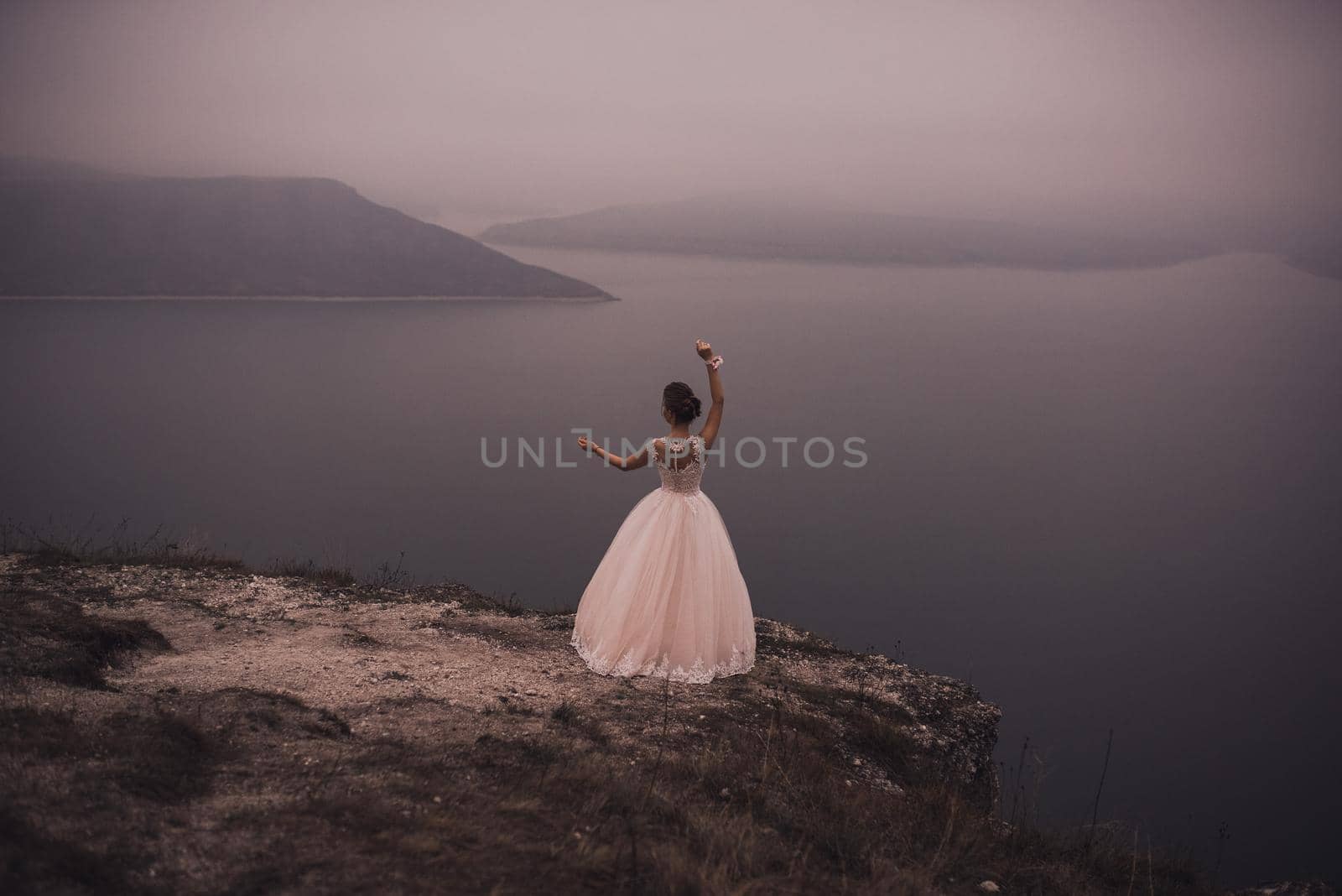 young slim beautiful woman Bride with a high Greek hairstyle and embellishment and in a White green puffy wedding dress stands on a cliff on top of a mountain. looks into the distance at sea the mount