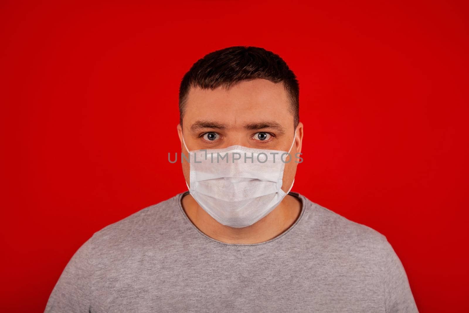 Portrait of a young man looking at the camera in a medical protective mask on a red background.