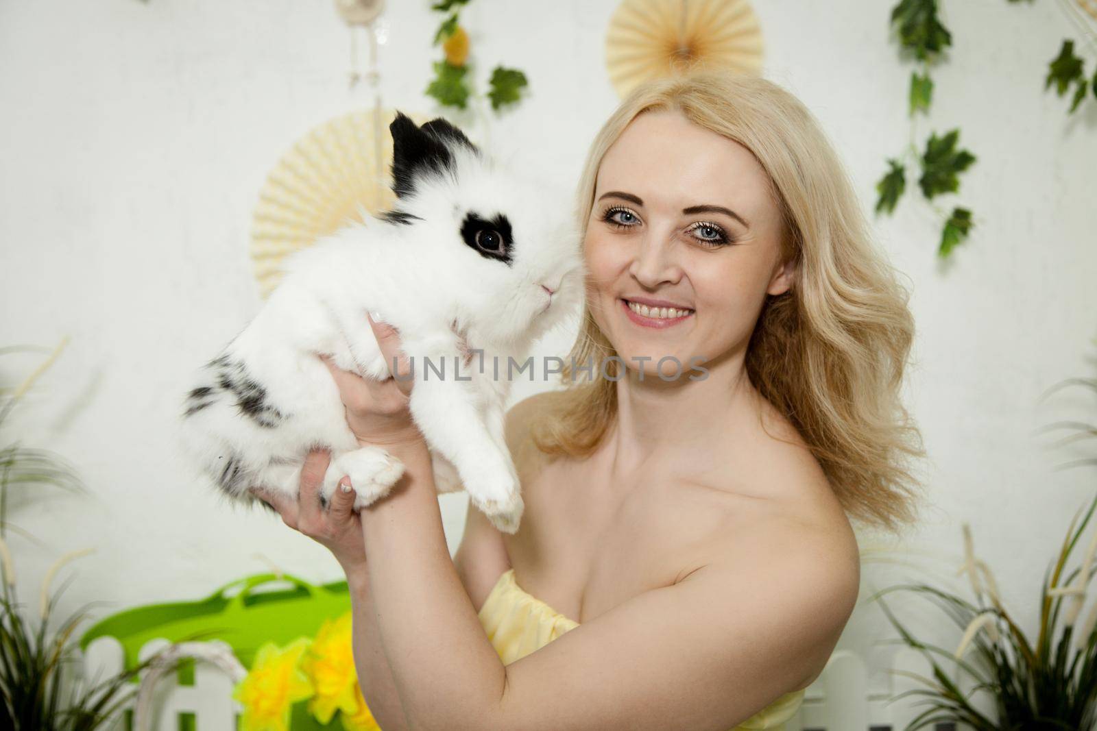 A lovely young blond woman standing in profile closeup and holding a young bunny in her arms. Beautiful blonde girl holding a white rabbit in her arms. Easter bunny sitting in the arms of a girl