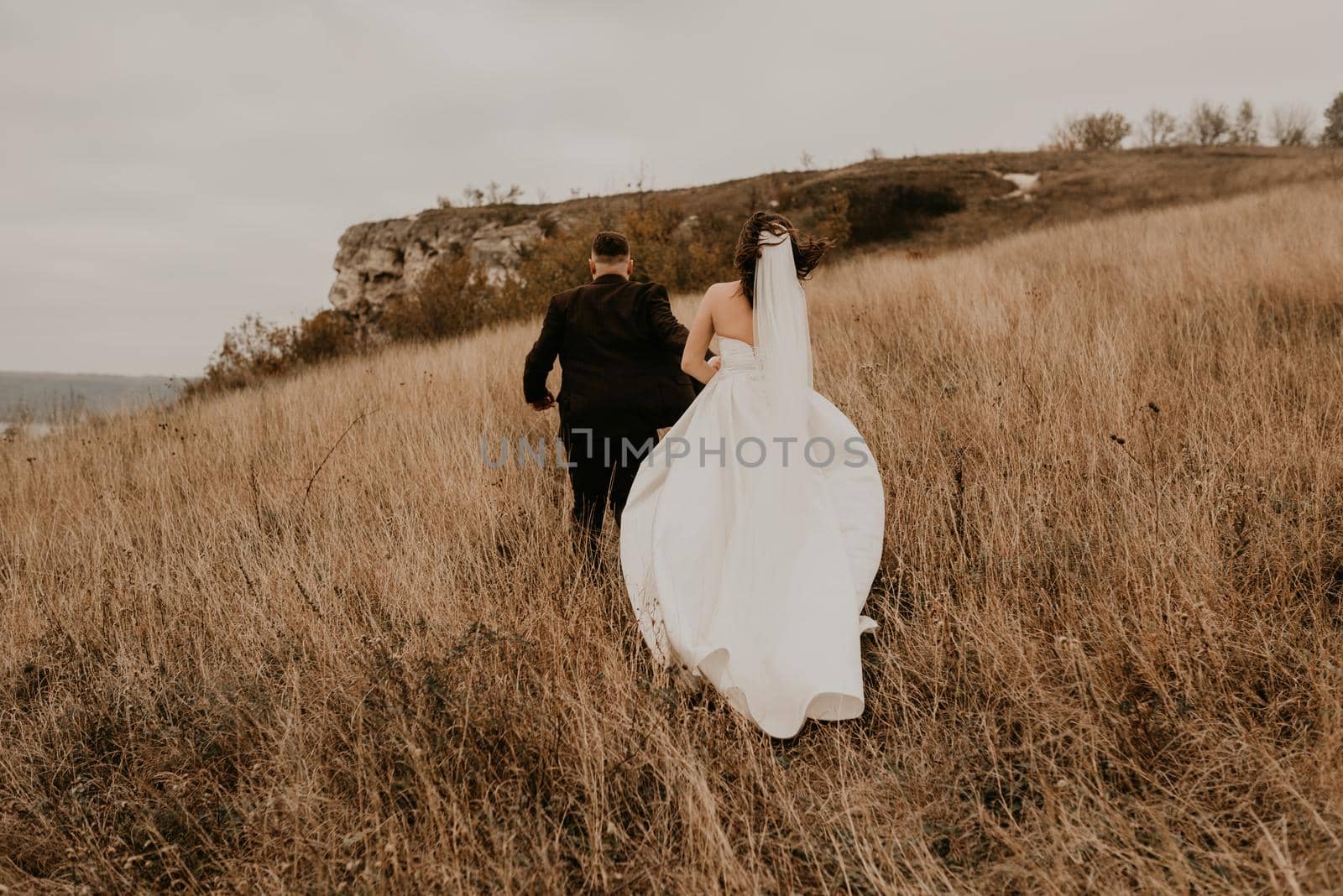 A loving couple wedding newlyweds in a white dress and a suit walk run hug kissing on the tall grass in the summer autumn field on the mountain above the river. sunset. bakota ukraine