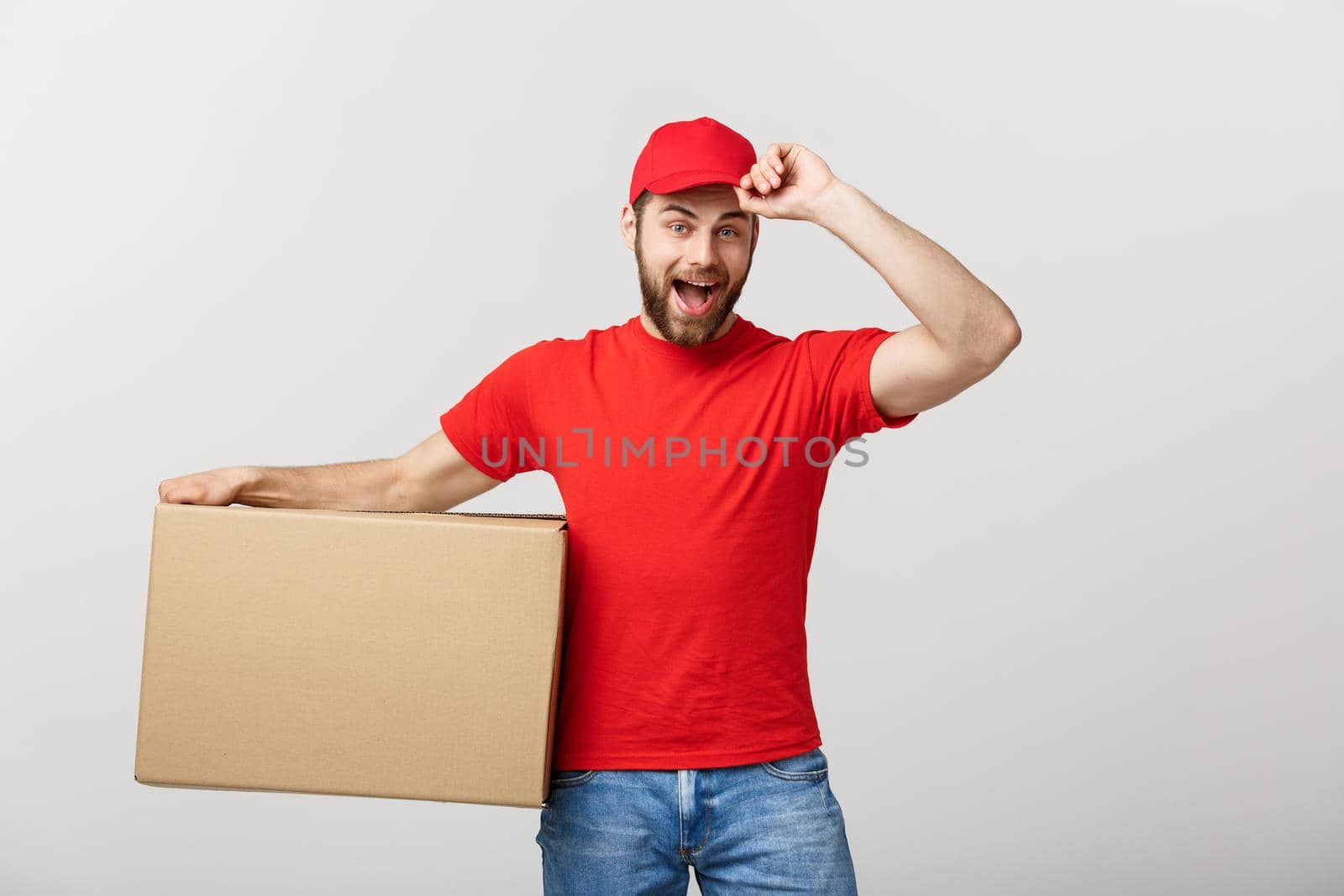 Deliver Concept: Young caucasian handsome delivery man holding a box on shoulder. Isolated over grey background