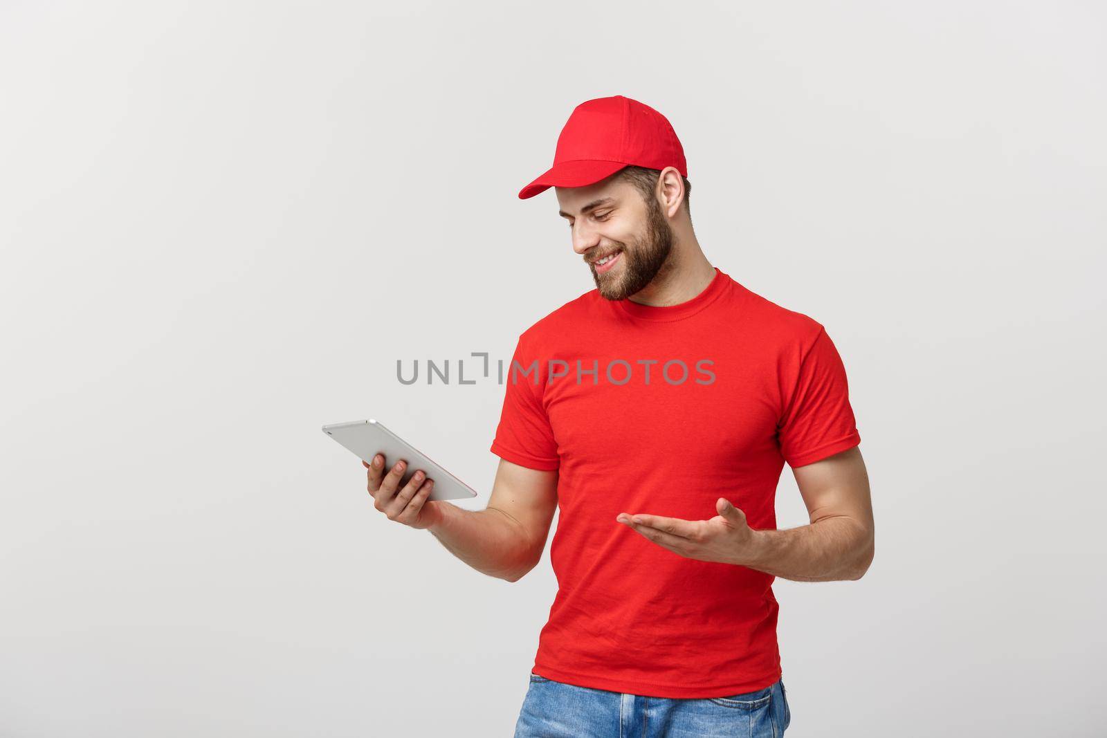 Smiling delivery man with tablet in studio. isolated gray background.