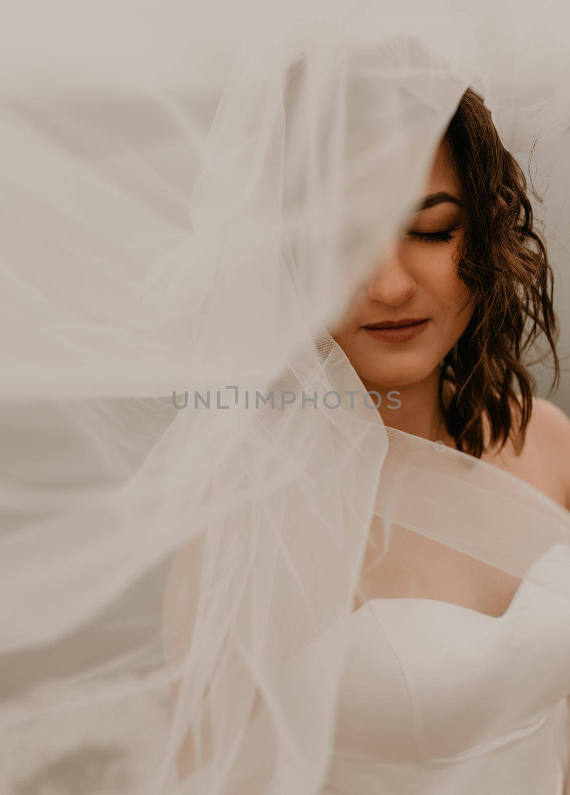 young brunette bride woman with short haircut in white wedding corset dress strapless and with a long chiffon veil on head. natural light nude makeup. Cool autumn weather. background large lake river