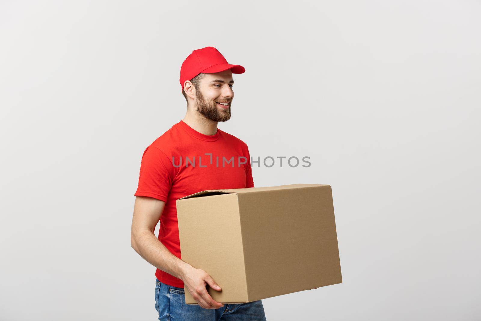 Young smiling logistic delivery man in red uniform holding the box on white background.