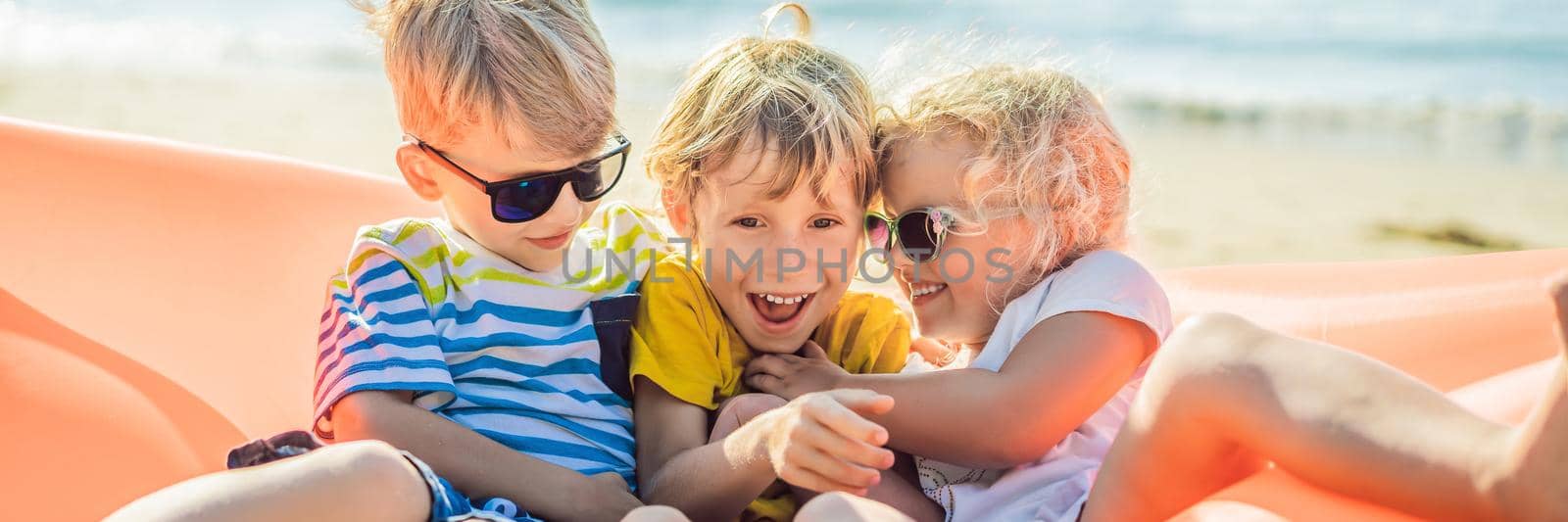 Children sit on an inflatable sofa against the sea and have fun. BANNER, LONG FORMAT