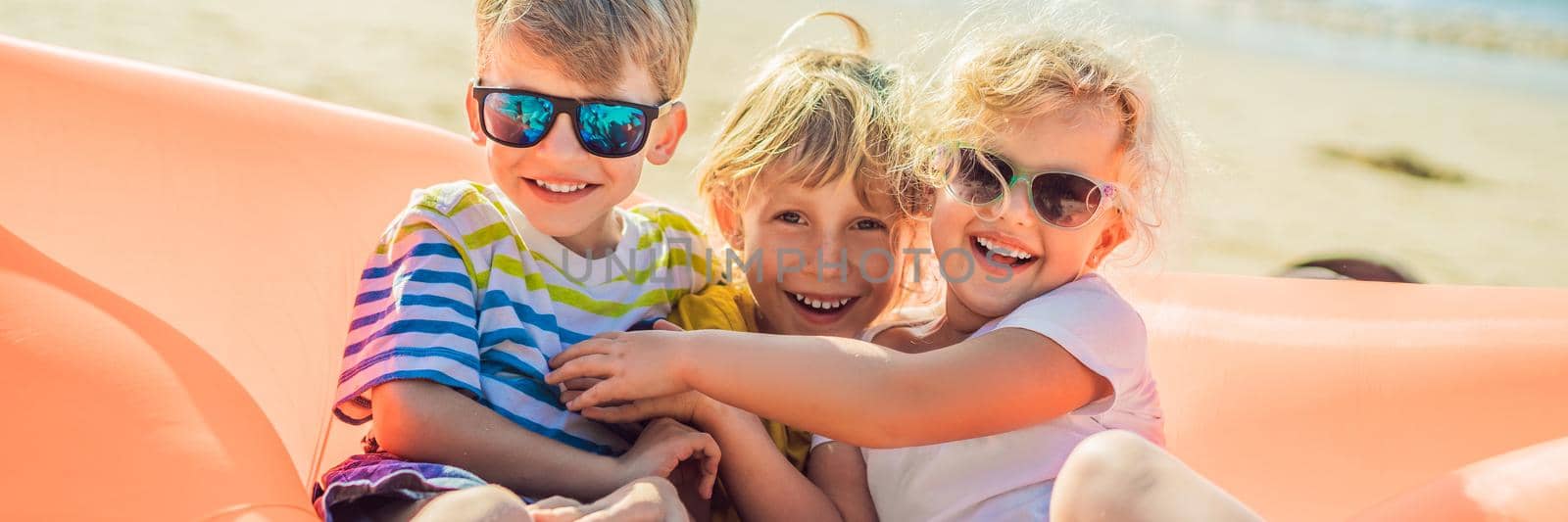 Children sit on an inflatable sofa against the sea and have fun. BANNER, LONG FORMAT