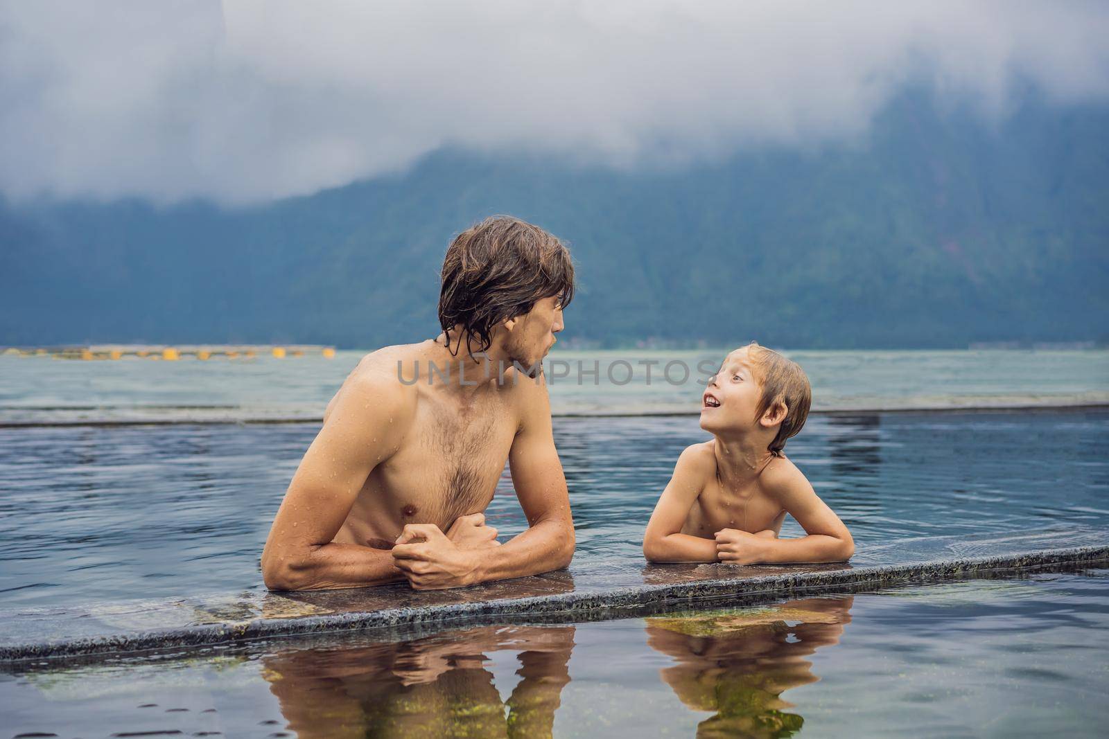 Dad and son travelers in Hot Springs in Bali on the background of lake. Traveling with children concept.
