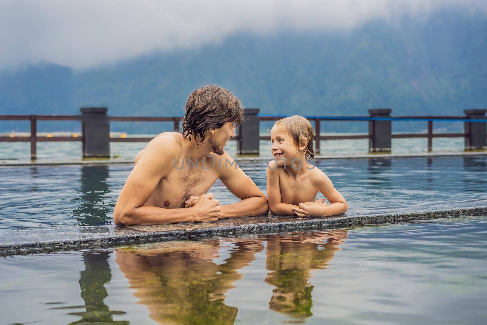 Dad and son travelers in Hot Springs in Bali on the background of lake. Traveling with children concept.