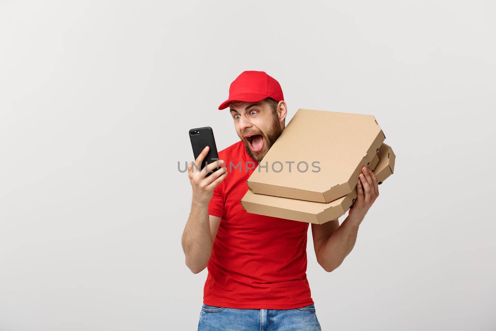Delivery Concept: Handsome pizza delivery man talking to mobile with shocking facial expression. Isolated over grey background