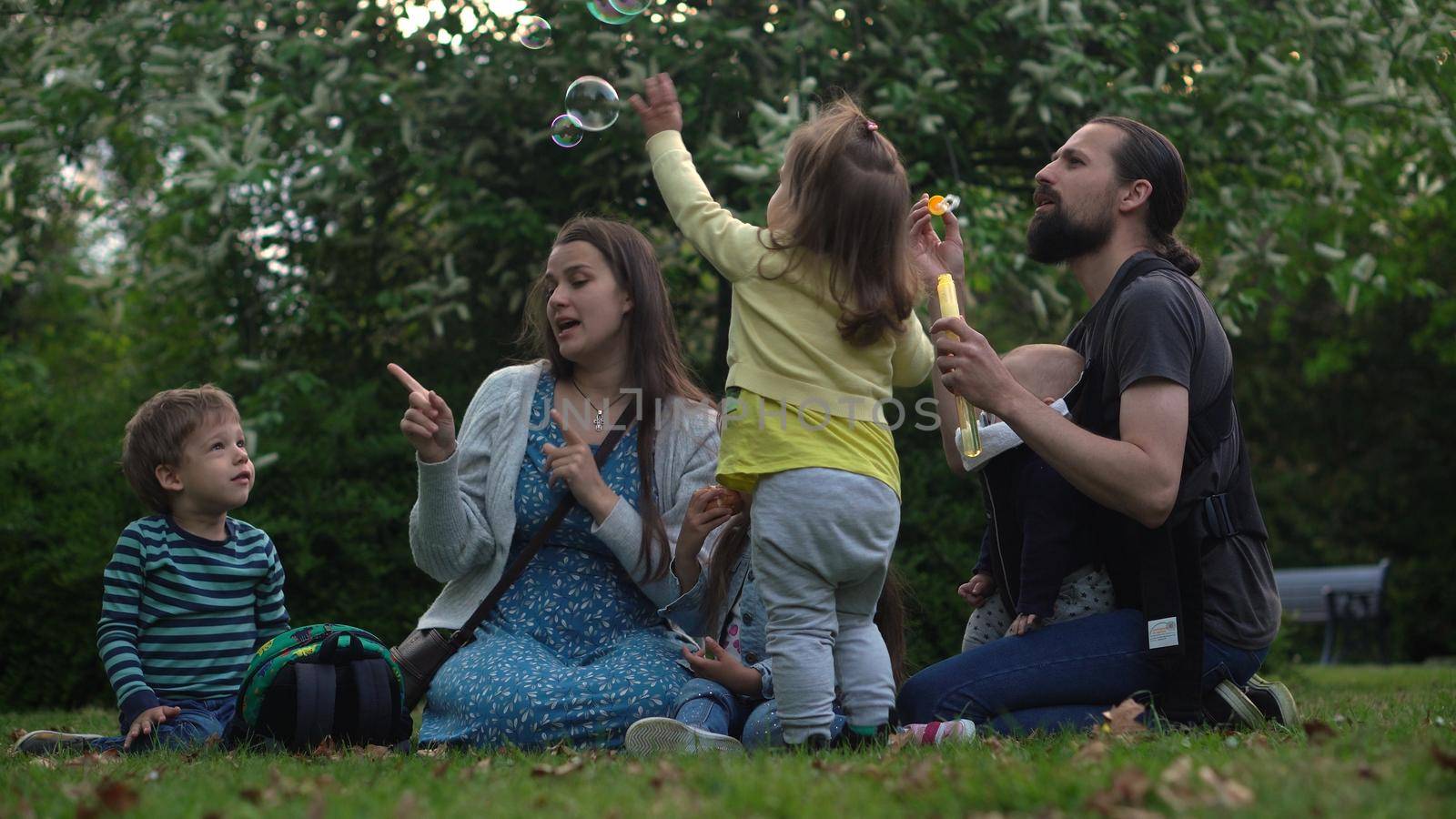 Happy family mother Father Three four Baby little siblings kids have fun blowing bubbles enjoying summer holidays in garden park. Smiling parents children spending leisure time together evening sunset.