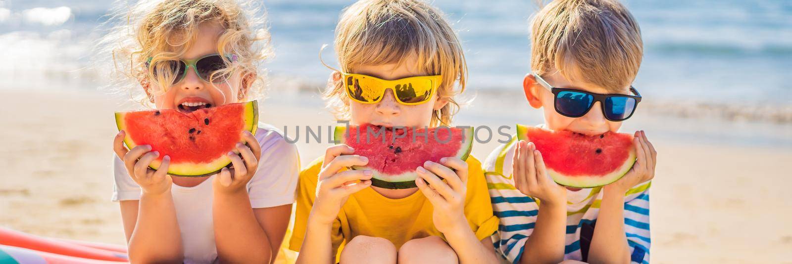 Children eat watermelon on the beach in sunglasses. BANNER, LONG FORMAT