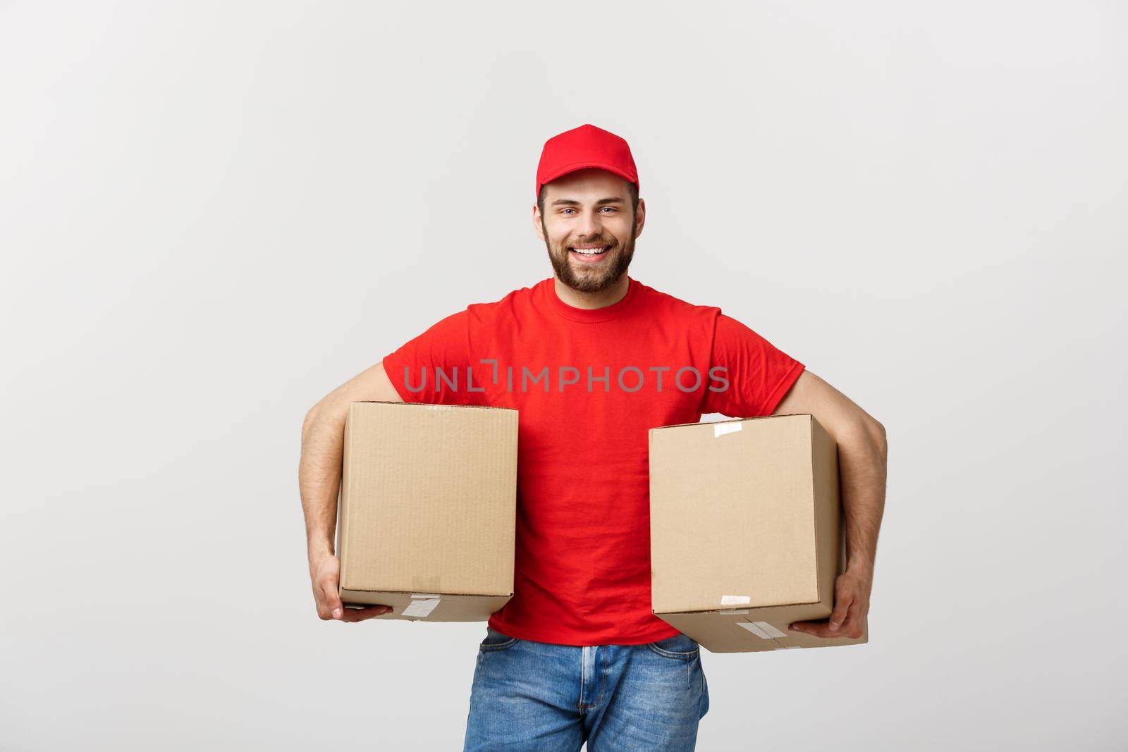 Delivery Concept: Smiling handsome caucasian delivery man holding a paper box. Isolated over grey background. by Benzoix
