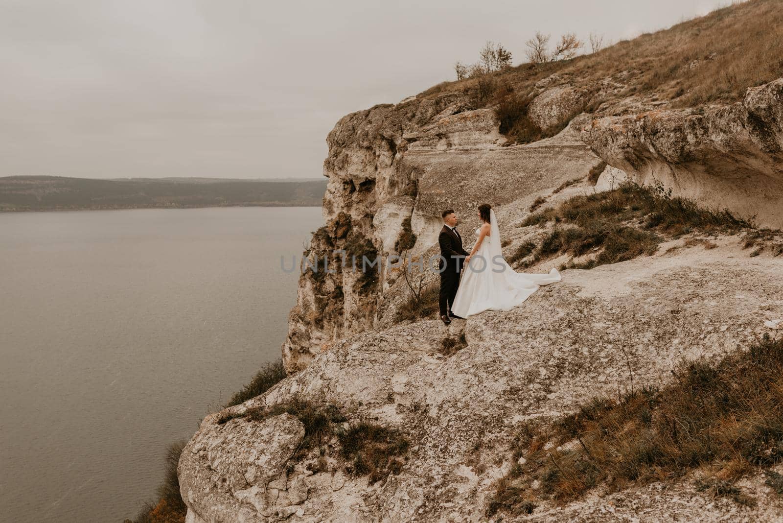 loving couple wedding newlyweds outdoor. bride in white dress long veil and groom in suit walk in summer fall on mountain above river. sunrise. man and woman on rocks above cliff. bakota ukraine