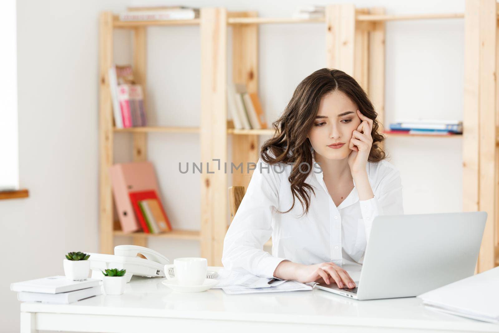 Young attractive woman at a modern office desk, working with laptop and thinking about something. by Benzoix