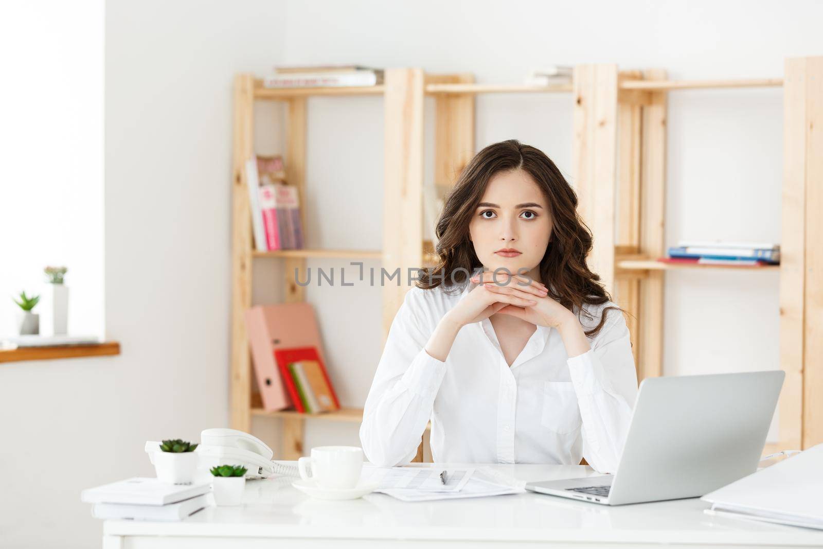 Young attractive woman at a modern office desk, working with laptop and thinking about something