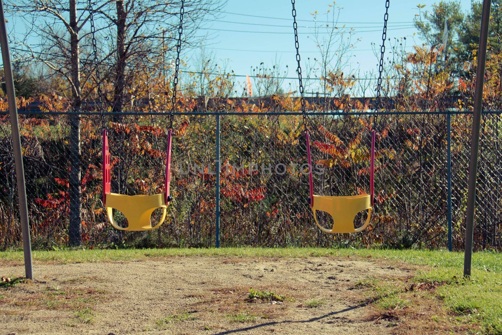 Bright yellow and red chain swings on kids playground. Autumn leaves. Covid restrictions by JuliaDorian