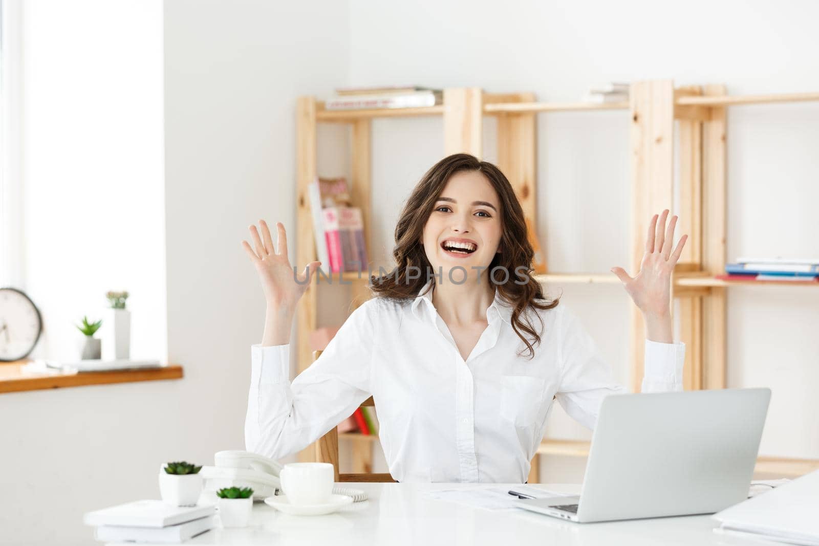 Successful business woman with arms up sitting in modern office. by Benzoix