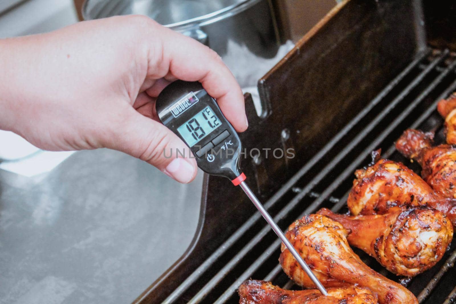 Gatineau, Quebec Canada - July 18, 2020: A food thermometer checking that chicken is being cooked correctly, safely on a barbecue along with prawns on a sunny day in the garden. Weber thermometer