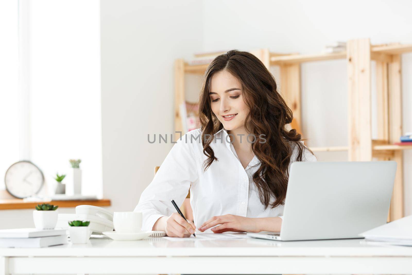 Portrait of a charming businesswoman sitting at her workplace and writing by Benzoix