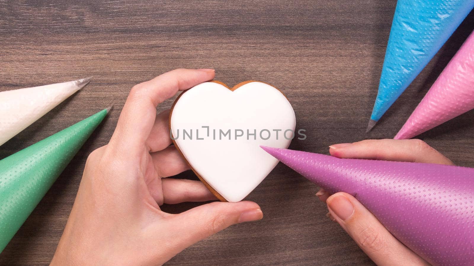 Hand holding white heart shape cookie with icing cone for Mothers day, Womans day or Valentines Day on wooden background. Copy space.