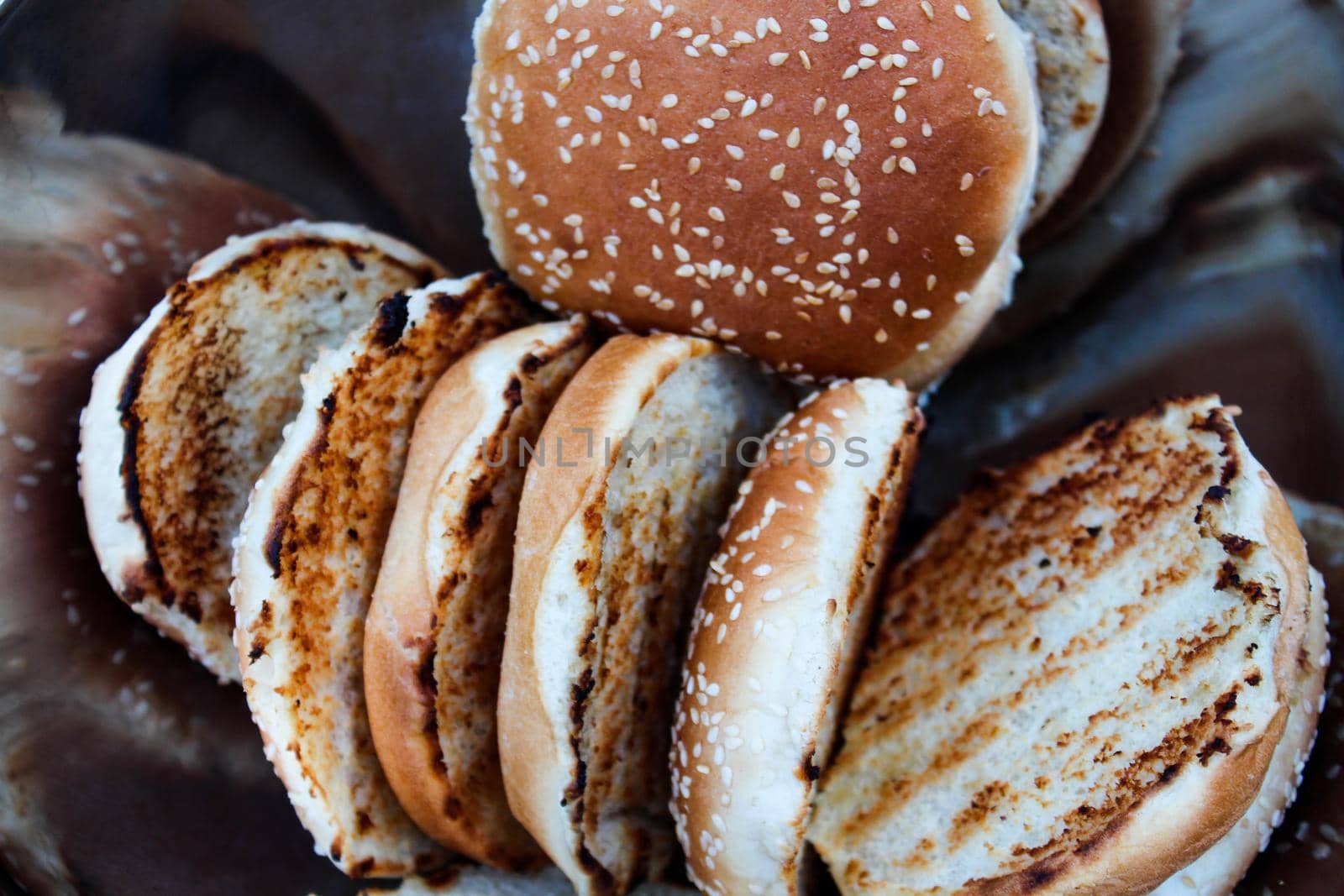 Grilled burger buns with sesame seeds in a metal bowl. by JuliaDorian