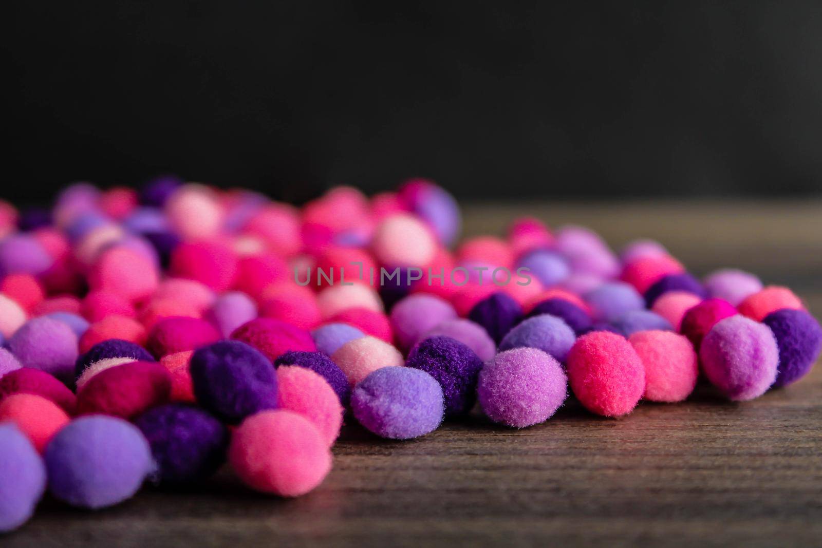 Round pink and purple fluffy balls pompoms on wooden background by JuliaDorian