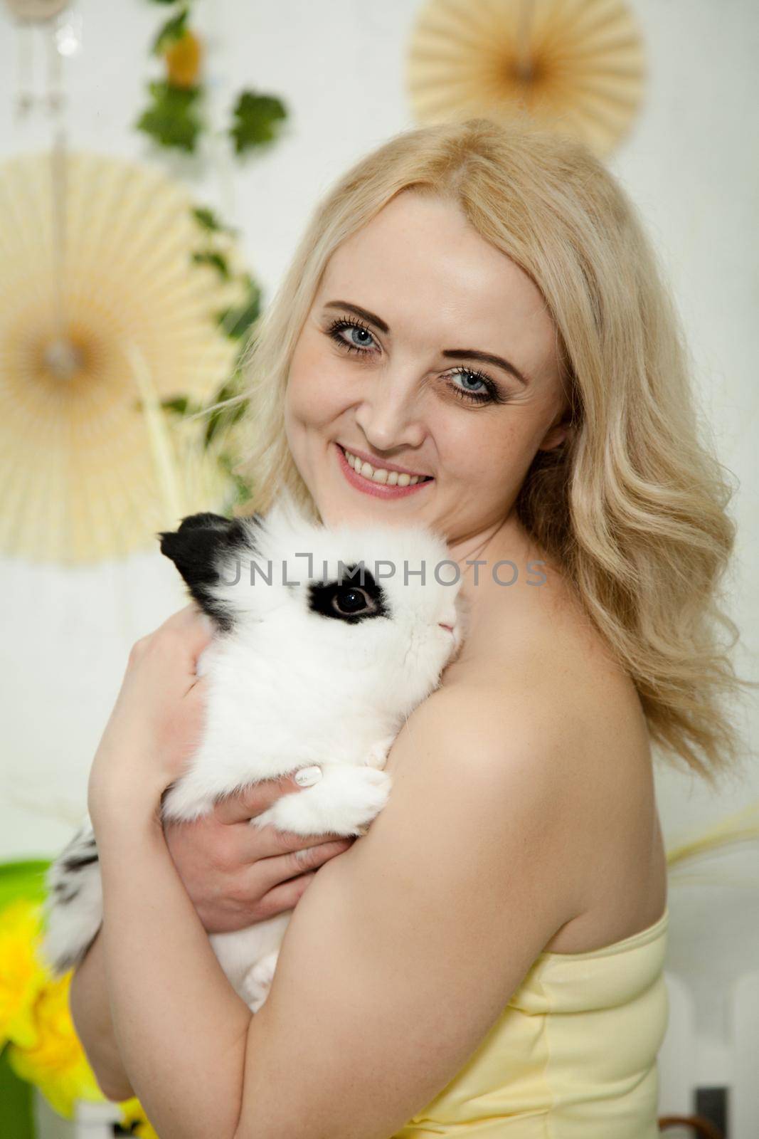 A lovely young blond woman standing in profile closeup and holding a young bunny in her arms. Beautiful blonde girl holding a white rabbit in her arms. Easter bunny sitting in the arms of a girl