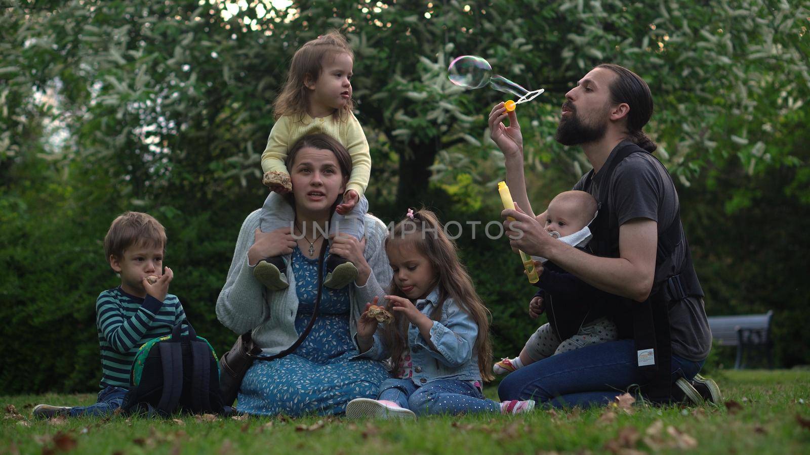 Happy family mother Father Three four Baby little siblings kids have fun blowing bubbles enjoying summer holidays in garden park. Smiling parents children spending leisure time together evening sunset.