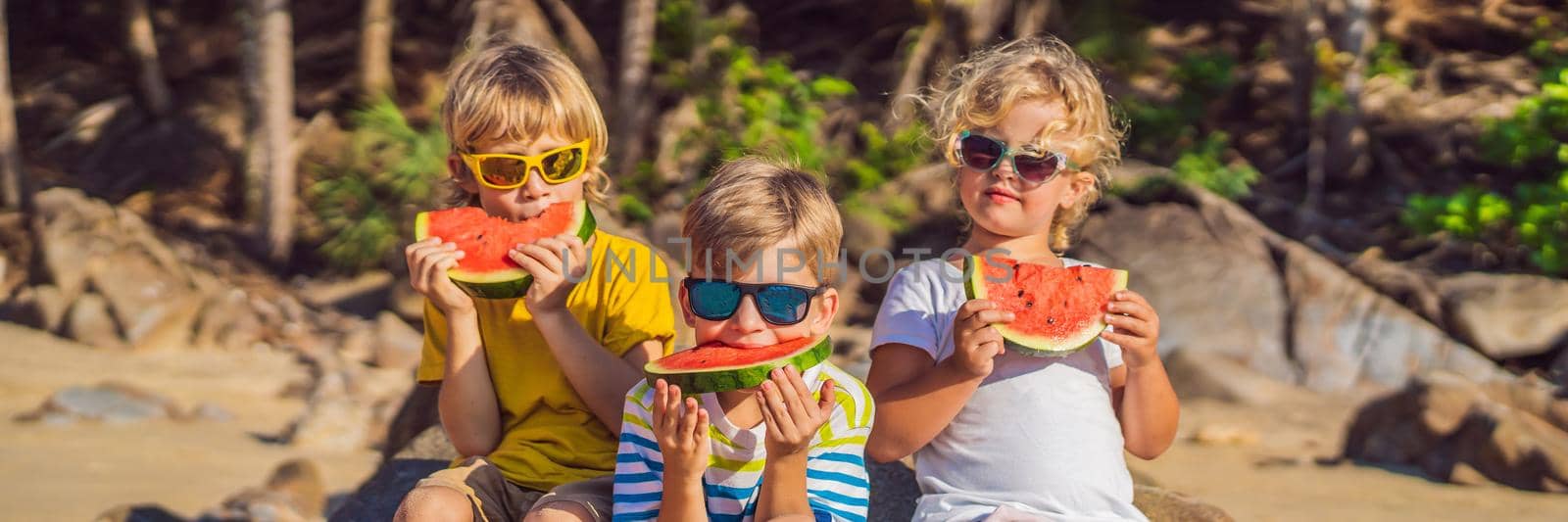 Children eat watermelon on the beach in sunglasses. BANNER, LONG FORMAT