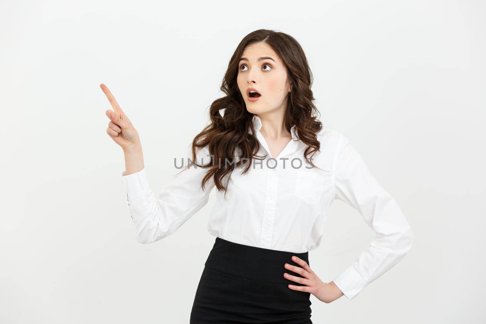 Business Concept: Portrait of surprised young businesswoman pointing finger away to copy space. Isolated on a white background