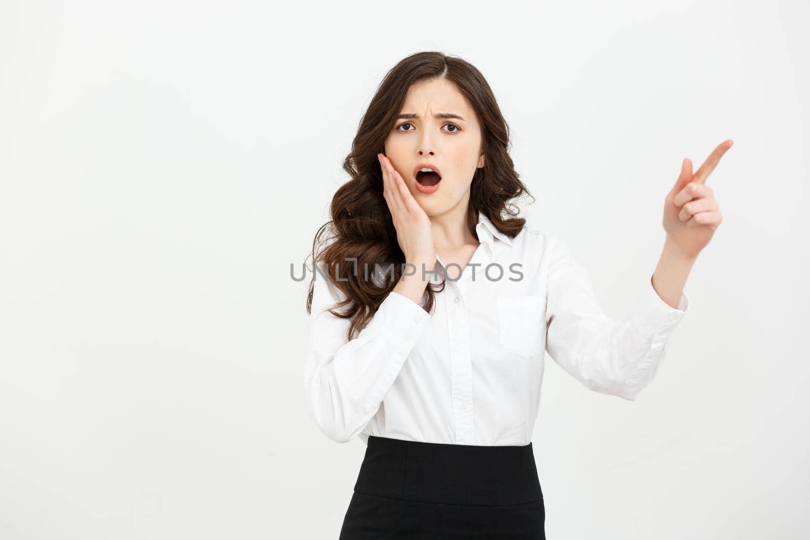 Business Concept: Portrait of surprised young businesswoman pointing finger away to copy space. Isolated on a white background