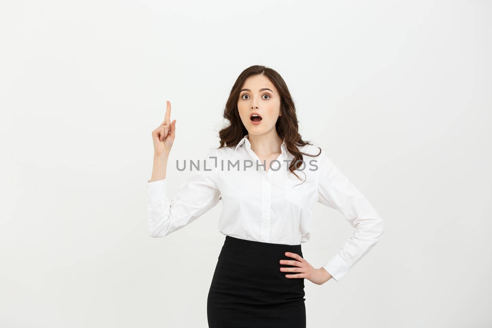 Business Concept: Attractive young Caucasian girl open her mouth and pointing her index finger to the top. She looks enthusiastic, isolated on white background.
