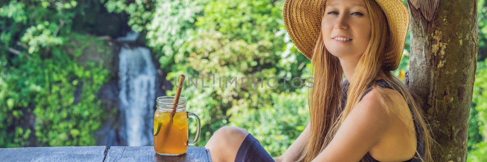 Closeup portrait image of a beautiful woman drinking ice tea with feeling happy in green nature and waterfall garden background. BANNER, LONG FORMAT