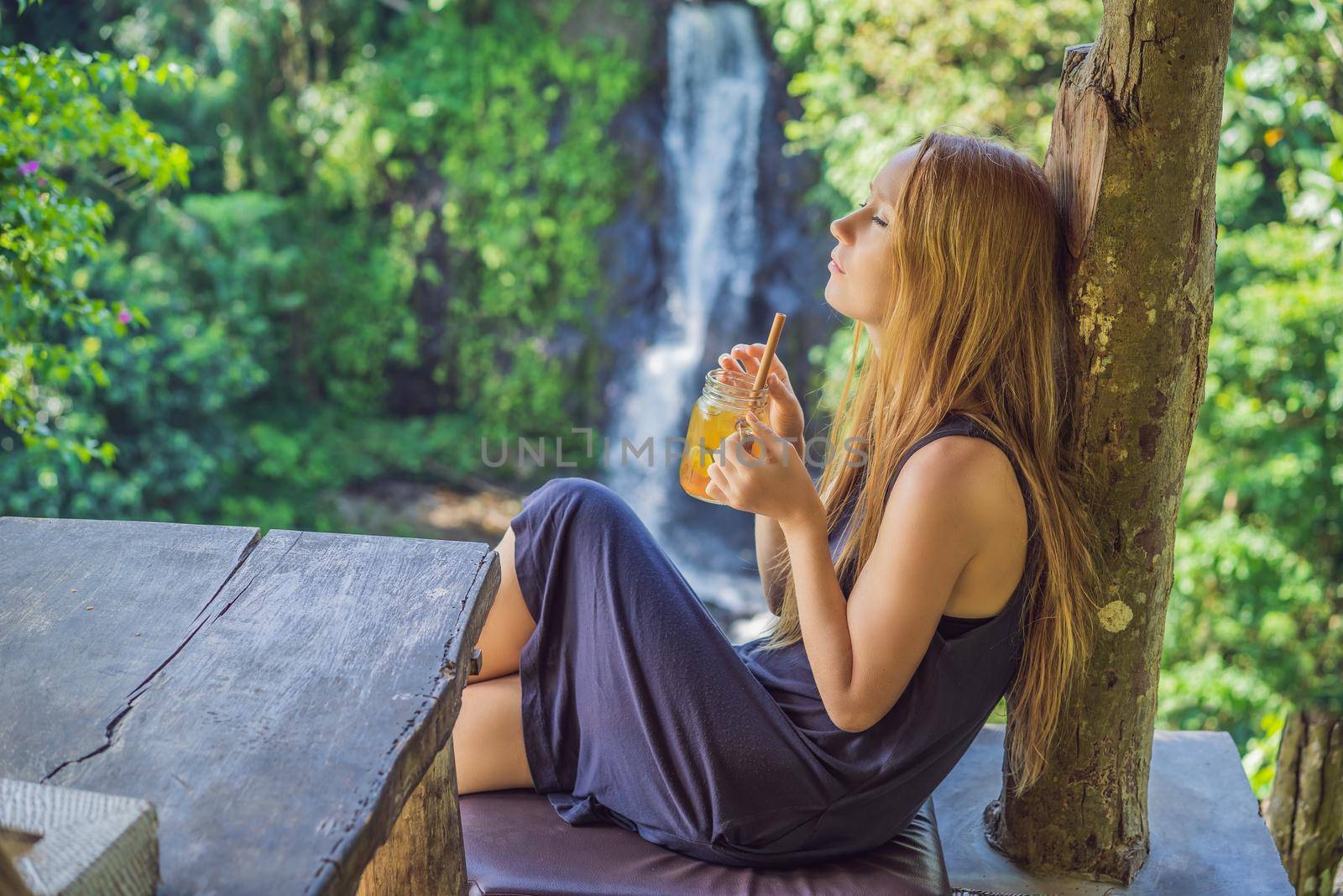 Closeup portrait image of a beautiful woman drinking ice tea with feeling happy in green nature and waterfall garden background.