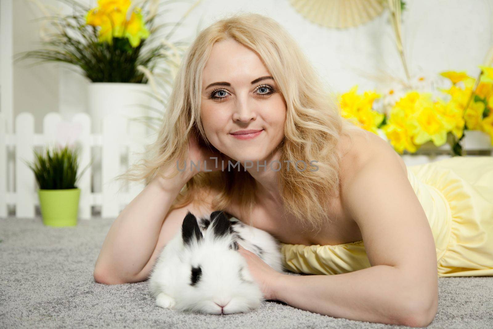 A lovely young blond woman standing in profile closeup and holding a young bunny in her arms. Beautiful blonde girl holding a white rabbit in her arms. Easter bunny sitting in the arms of a girl