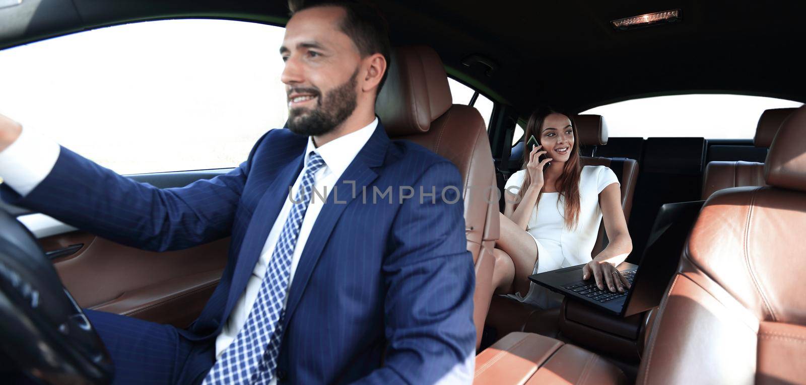 Businesswoman on the backseat with elegant man driving a car in the city.